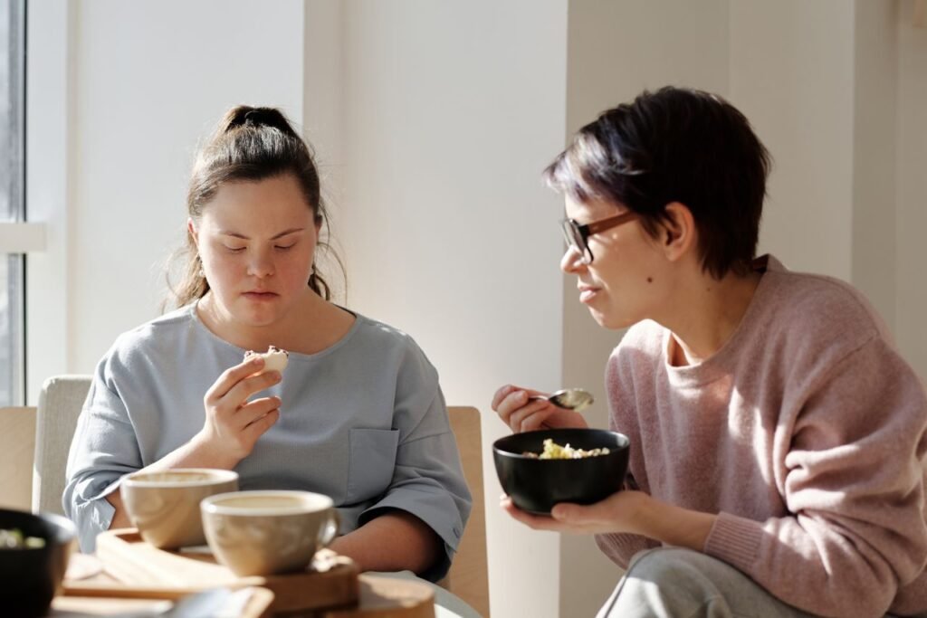 Being a Carer in the UK: Responsibilities, Rights and Support Two women sharing breakfast, one with Down syndrome, fostering togetherness and care.